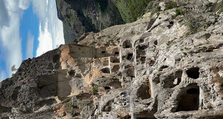 Ciudad cueva espectacular en el acantilado con múltiples viviendas excavadas en la roca y visitantes caminando por senderos estrechos sobre un exuberante valle.