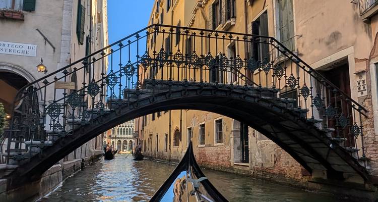 Vista desde la proa de la góndola del puente peatonal de hierro ornamentado que se arquea sobre el estrecho canal veneciano