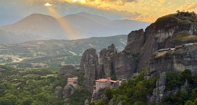 Un rayon de soleil dramatique perçant les nuages au-dessus des pics rocheux de Meteora et du monastère.