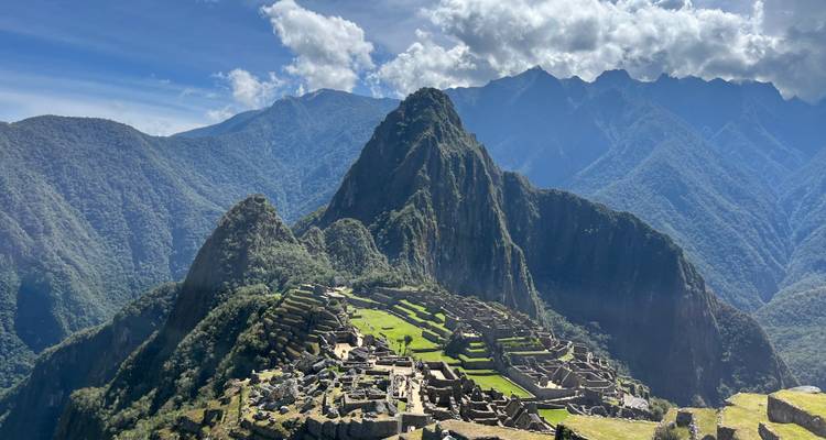 Vista clásica de postal de las ruinas de Machu Picchu y los picos circundantes bajo nubes dispersas.