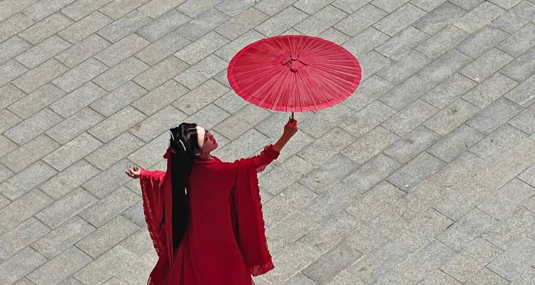 Mujer con un vestido rojo tradicional y fluyente sosteniendo un paraguas rojo, vista desde arriba