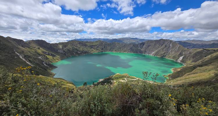 Emerald water fills the volcanic crater lake of Quilotoa under a vibrant blue sky.