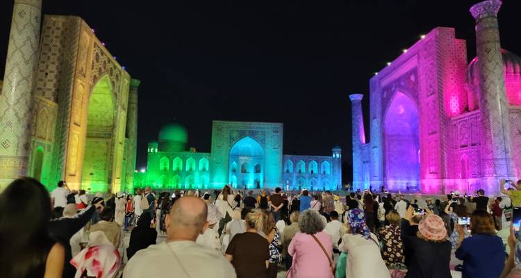 El espectáculo de luces nocturno baña el Registan de Samarcanda con colores vibrantes mientras la multitud observa.