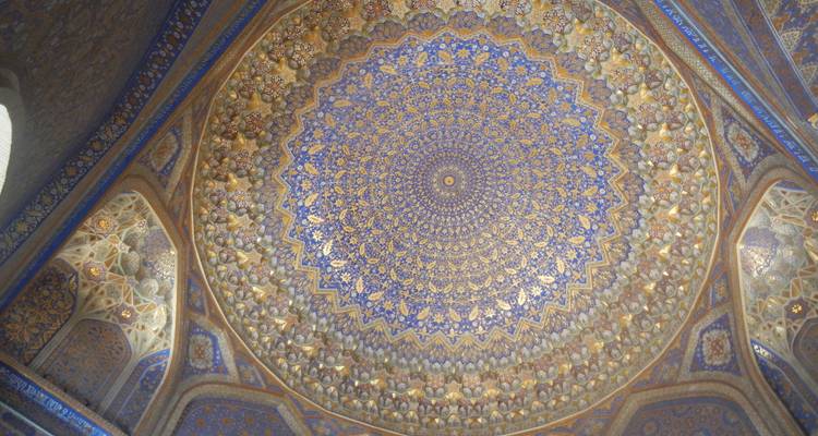 Techo de cúpula islámica azul y dorado intricadamente decorado con patrones geométricos simétricos.