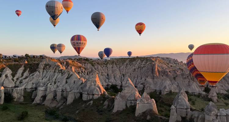 Meerdere kleurrijke luchtballonnen zweven over zonbeschenen feeënschouwen tijdens het gouden uur in Cappadocië.