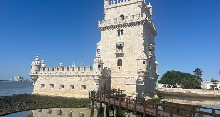 Iconische stenen Belém Tower die uit de rivierrand omhoog rijst met een houten voetgangersbrug en een levendige blauwe lucht