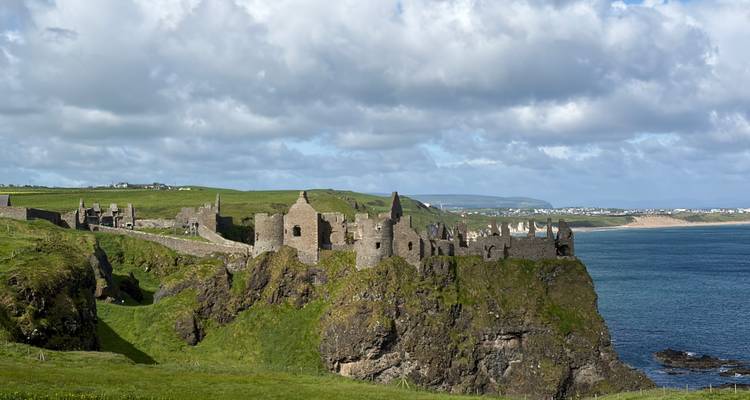Les ruines de pierre d'un château médiéval se dressent sur des falaises verdoyantes surplombant une mer d'un bleu profond.