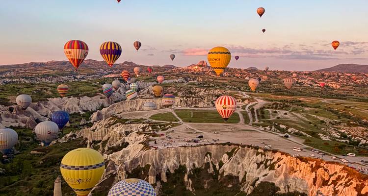 Tientallen kleurrijke luchtballonnen drijven bij zonsopgang boven de unieke rotsvalleien van Cappadocië.