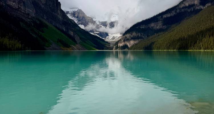 El icónico Lago Louise de color turquesa reflejando glaciares brumosos y picos escarpados bajo un cielo sombrío
