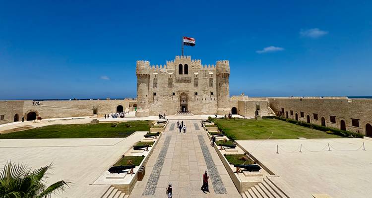 Fort Qaitbay domina un soleado patio junto al agua con visitantes paseando abajo.