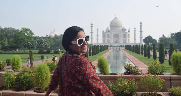 Una mujer con un vestido estampado mira hacia atrás sonriendo con el reflejo del estanque que lleva hacia el Taj Mahal.
