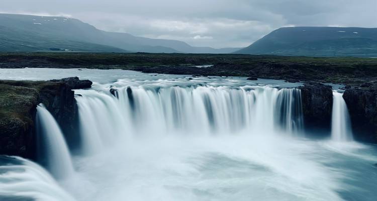 Langzeitbelichtungsfotografie eines breiten Wasserfalls, der in eine neblige Schlucht unter bewölktem Himmel stürzt.