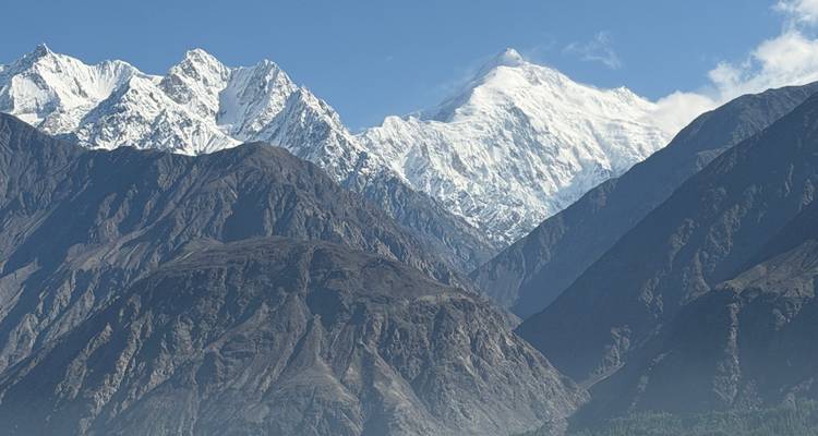 Les pics montagneux enneigés s'élançant au-dessus des crêtes rocheuses sombres sous un ciel bleu clair