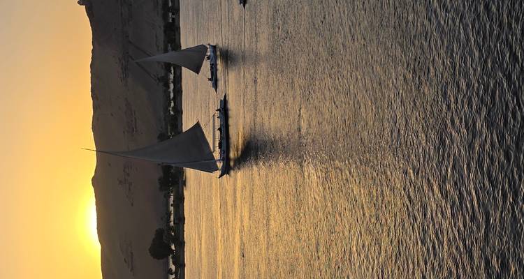 Deux felouques naviguant sur le Nil au coucher du soleil avec des reflets dorés sur l'eau