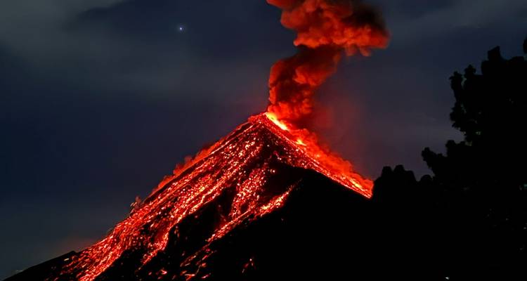 Éruption volcanique nocturne avec un fleuve de lave incandescente en cascade descendant la pente