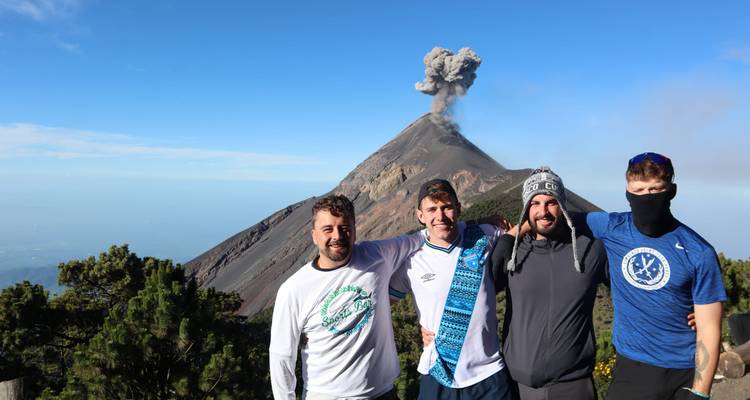 Groupe d'amis souriant avec un volcan en éruption dégageant de la cendre derrière eux