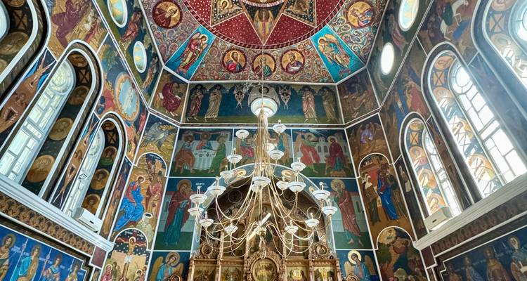 Interior de iglesia ortodoxa ricamente decorada con frescos coloridos y araña
