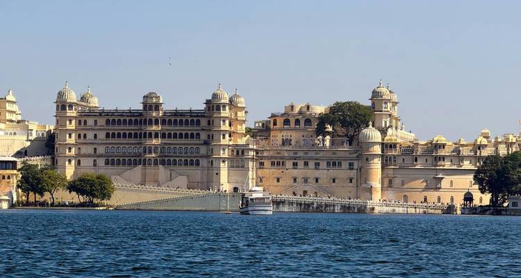 Le lac Pichola avec le grand complexe du Palais de la Ville d'Udaipur et un bateau touristique sur une eau bleue calme