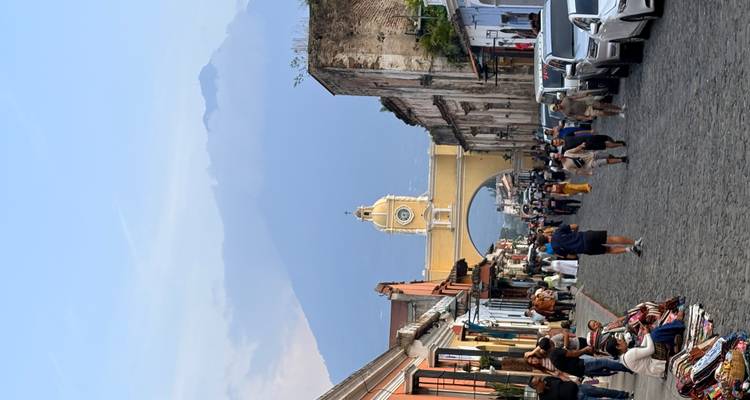 Cobblestone street of Antigua leads to the iconic yellow Santa Catalina Arch with looming volcano backdrop and bustling vendors.