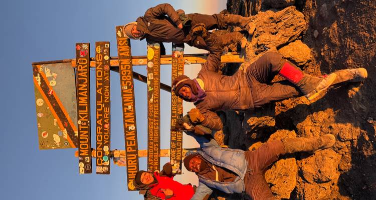 Climbers celebrate at Uhuru Peak sign with golden dawn light on the summit of Kilimanjaro