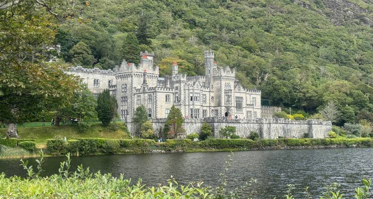 Victorian-era Kylemore Abbey reflected in a lake, surrounded by lush forested hills.