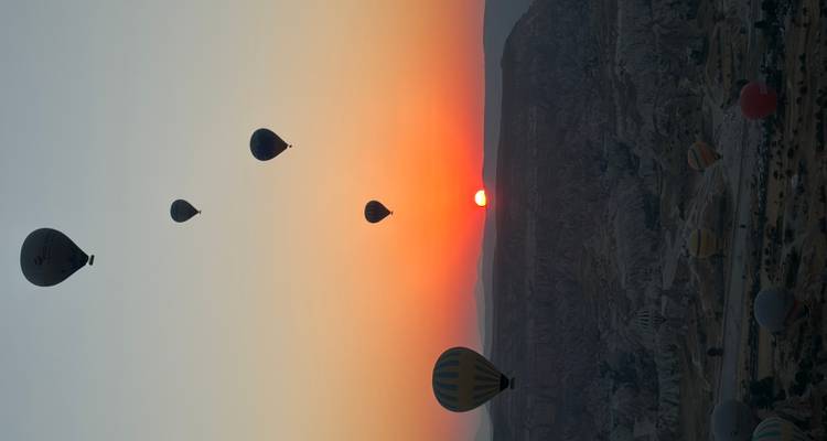 Globos aerostáticos recortados en silueta ascendiendo hacia un amanecer naranja vibrante sobre los valles rocosos de Capadocia.