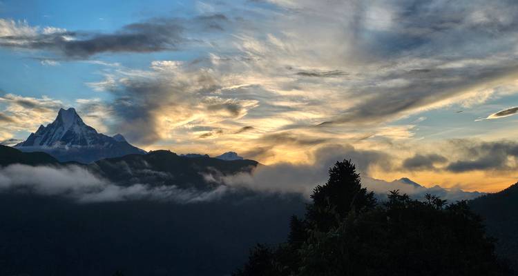 Les nuages spectaculaires du lever de soleil tourbillonnent au-dessus des pics enneigés de l'Himalaya tandis que la brume s'écoule dans une vallée profonde.