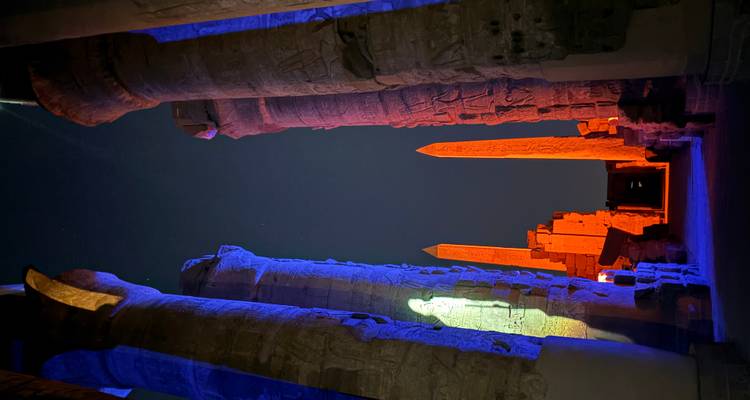 Nighttime view down a colonnaded temple corridor lit dramatically in blue and orange with two obelisks.