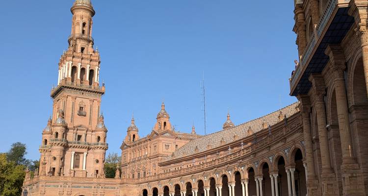 De toren van Plaza de España in Sevilla en de uitgestrekte zuilengang glinsterend in het late middaglicht tegen een helder lucht.