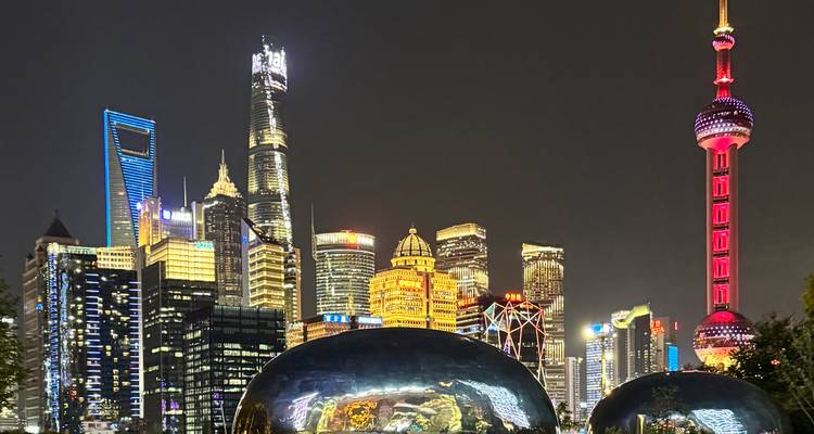 Nighttime view of Shanghai’s illuminated skyline featuring the Oriental Pearl Tower and mirrored sculptures in the foreground.