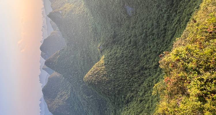 Sweeping golden-hour vista of green karst mountains and valleys stretching into the hazy distance.