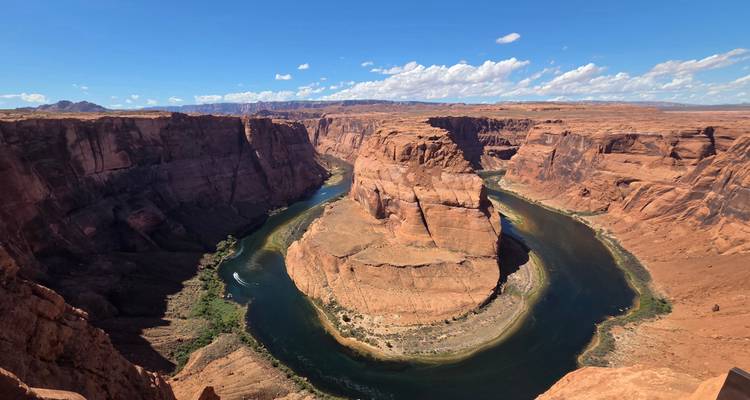 A sweeping view of Horseshoe Bend shows the emerald Colorado River looping around a sheer sandstone mesa beneath a bright sky.