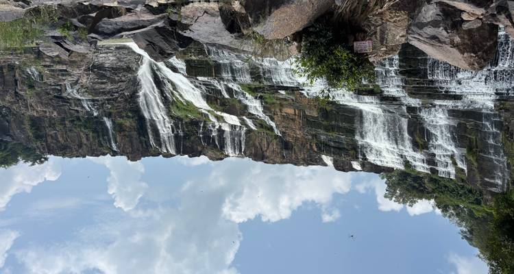 Cascada amplia de múltiples niveles cayendo sobre formaciones rocosas oscuras bajo un cielo azul con nubes