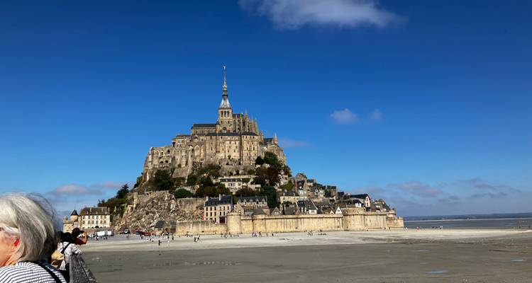 Iconic Mont Saint-Michel rising above vast tidal flats beneath a clear blue sky.