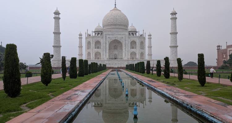 The Taj Mahal and its reflecting pool framed by manicured gardens on a hazy morning.