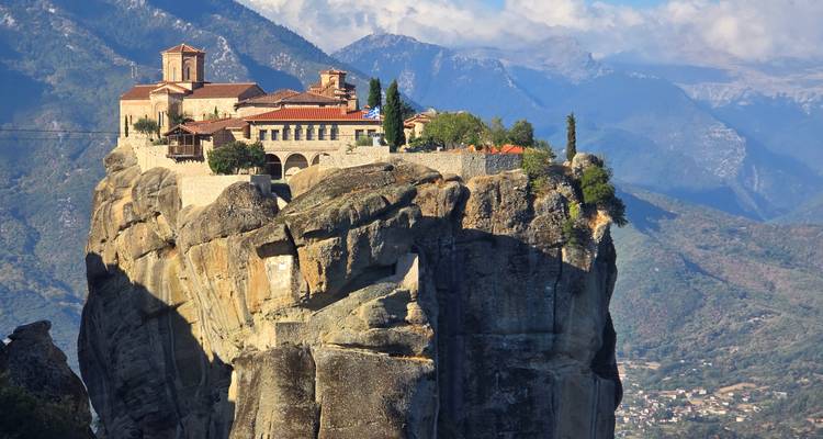 Monastery perched dramatically atop a towering rock column with layered mountains in the distance.