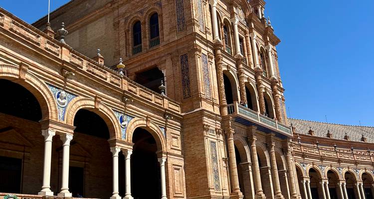 Tower and arched galleries of Plaza de España in warm sunlight against a clear blue sky.