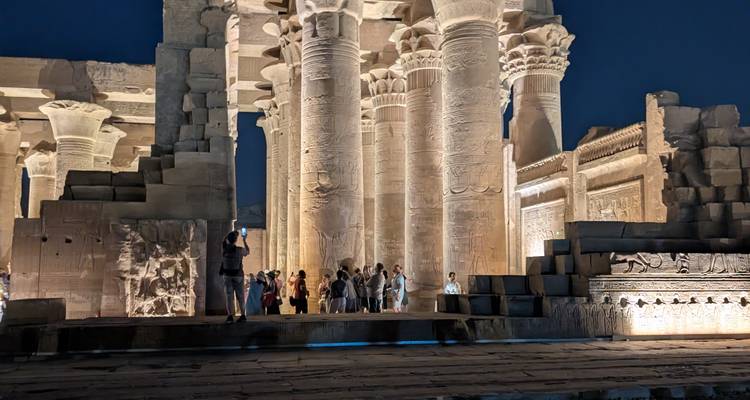 Iluminación nocturna de las columnas del templo de Kom Ombo con jeroglíficos intrincados y turistas abajo