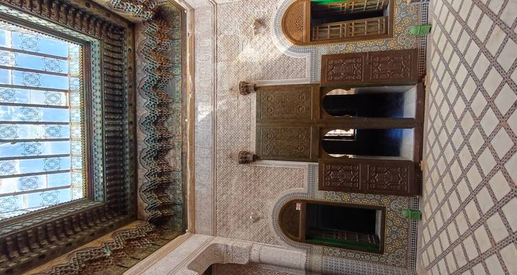 Patio interior con azulejos intrincados, techos de cedro tallado e iluminación natural en una madrasa marroquí.