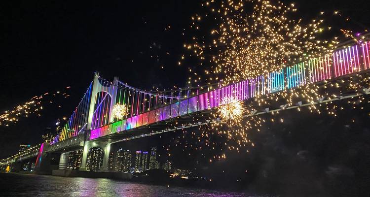 Fuegos artificiales nocturnos y un espectáculo de luces multicolor iluminando un largo puente colgante sobre el agua.
