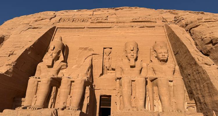 Colossal seated statues of Abu Simbel carved into desert cliff face glow in warm light.