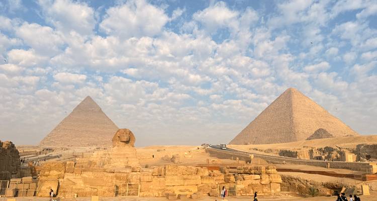 Panoramic view of the Great Pyramids and Sphinx under a dramatic cloud-studded sky.