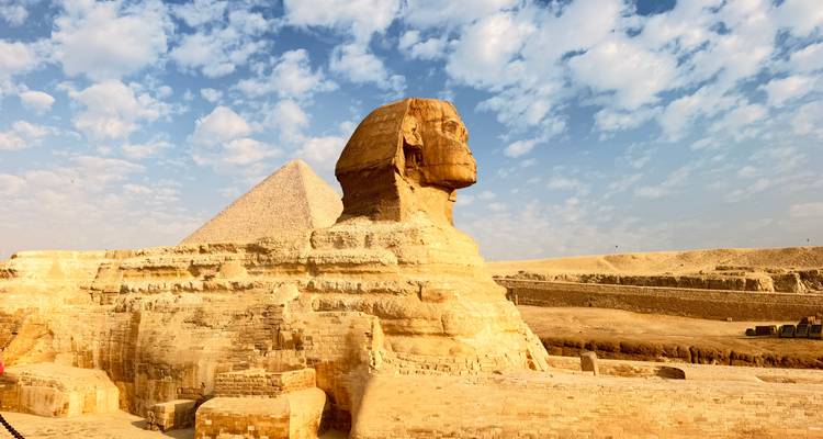 Close-up of the Sphinx profile with pyramid backdrop against a bright sky.