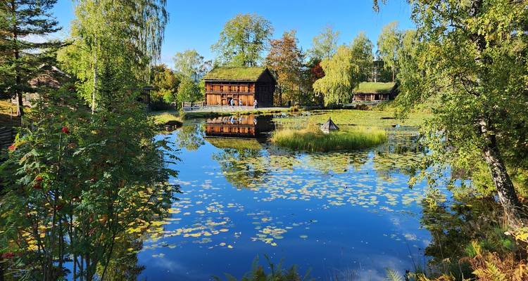 A rural house reflected in a tranquil pond surrounded by trees.