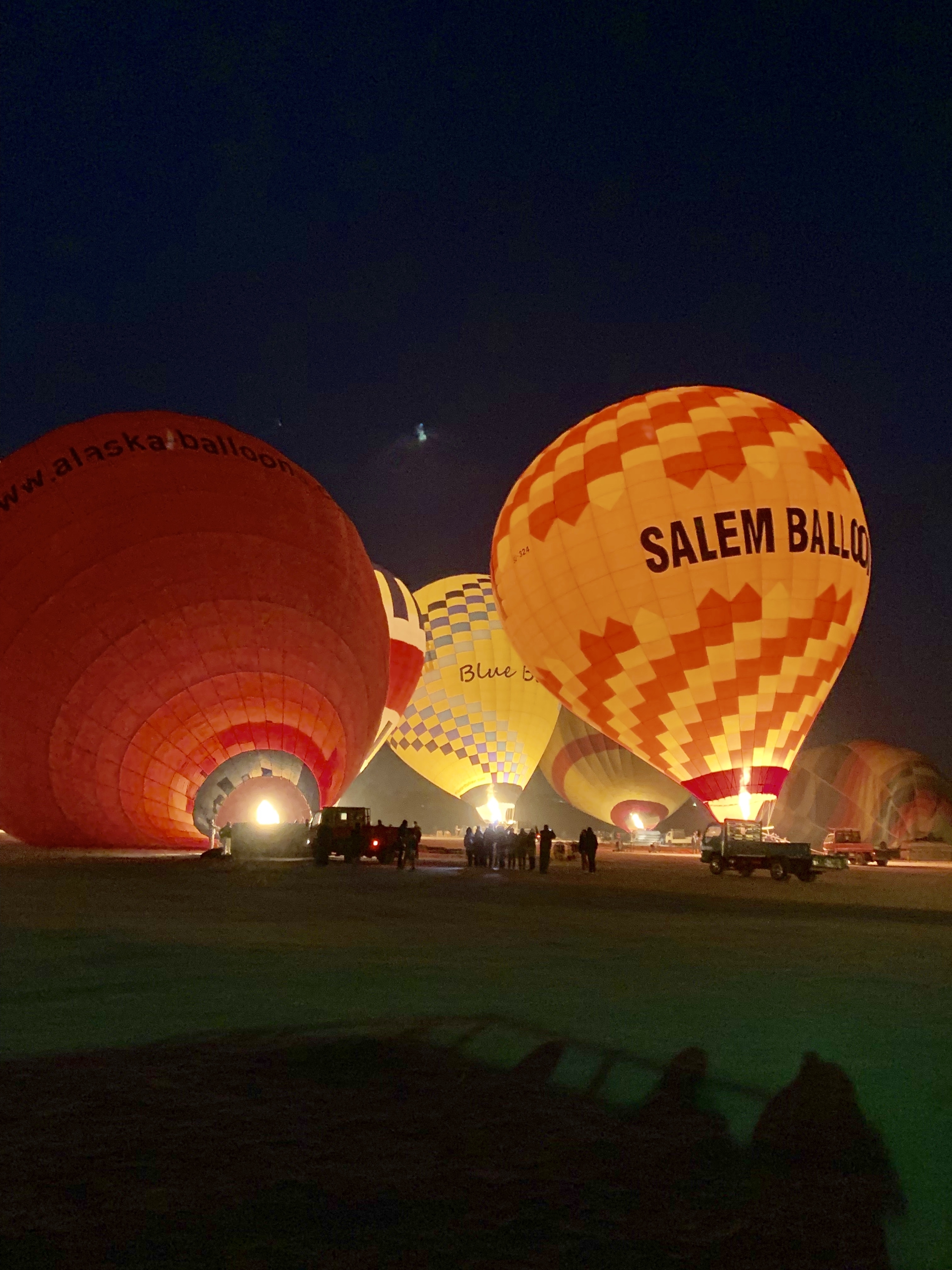 Hot air balloons illuminated at night with a group of people nearby.