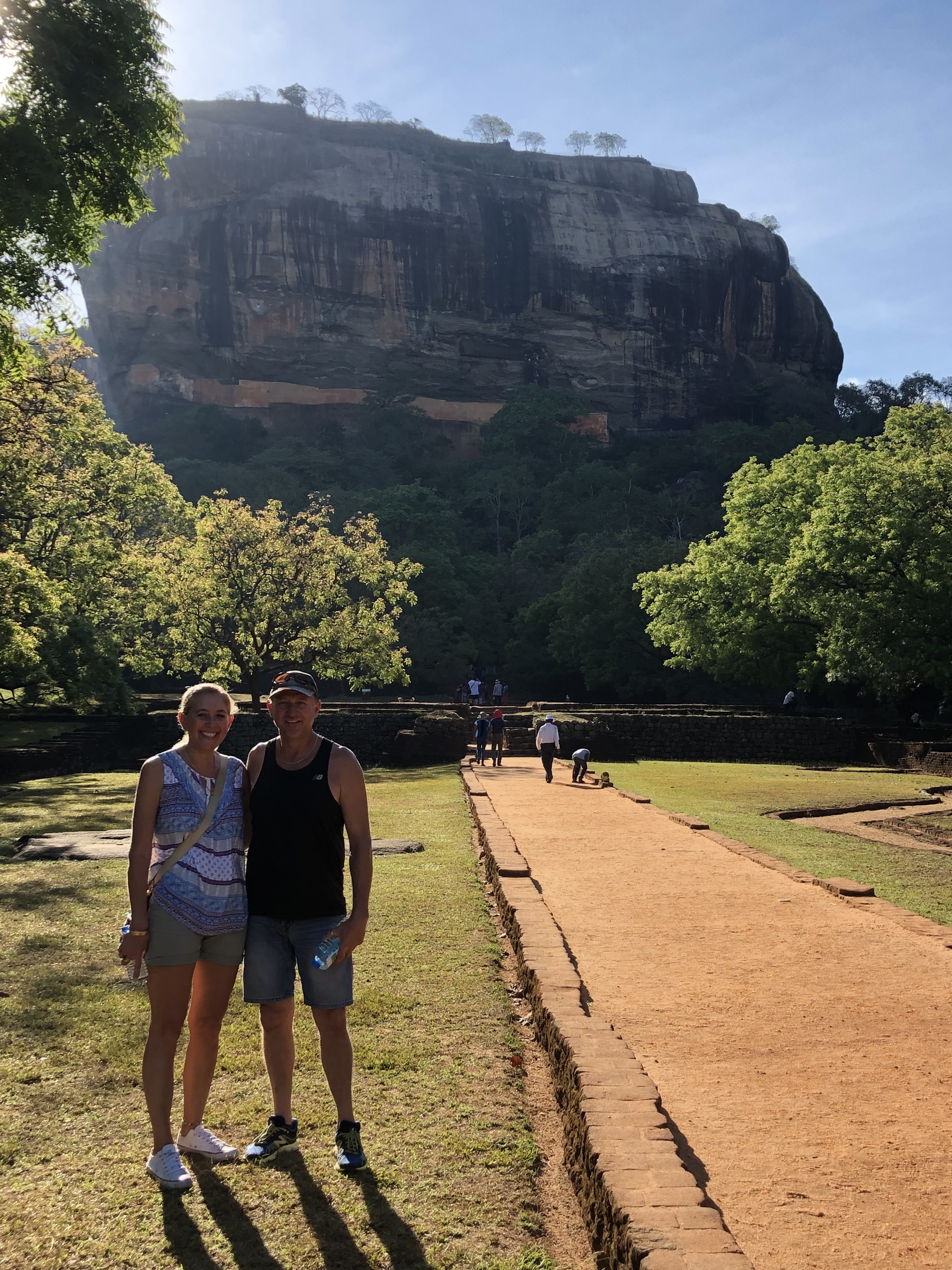 Couple posing in front of a historical site with lush trees.