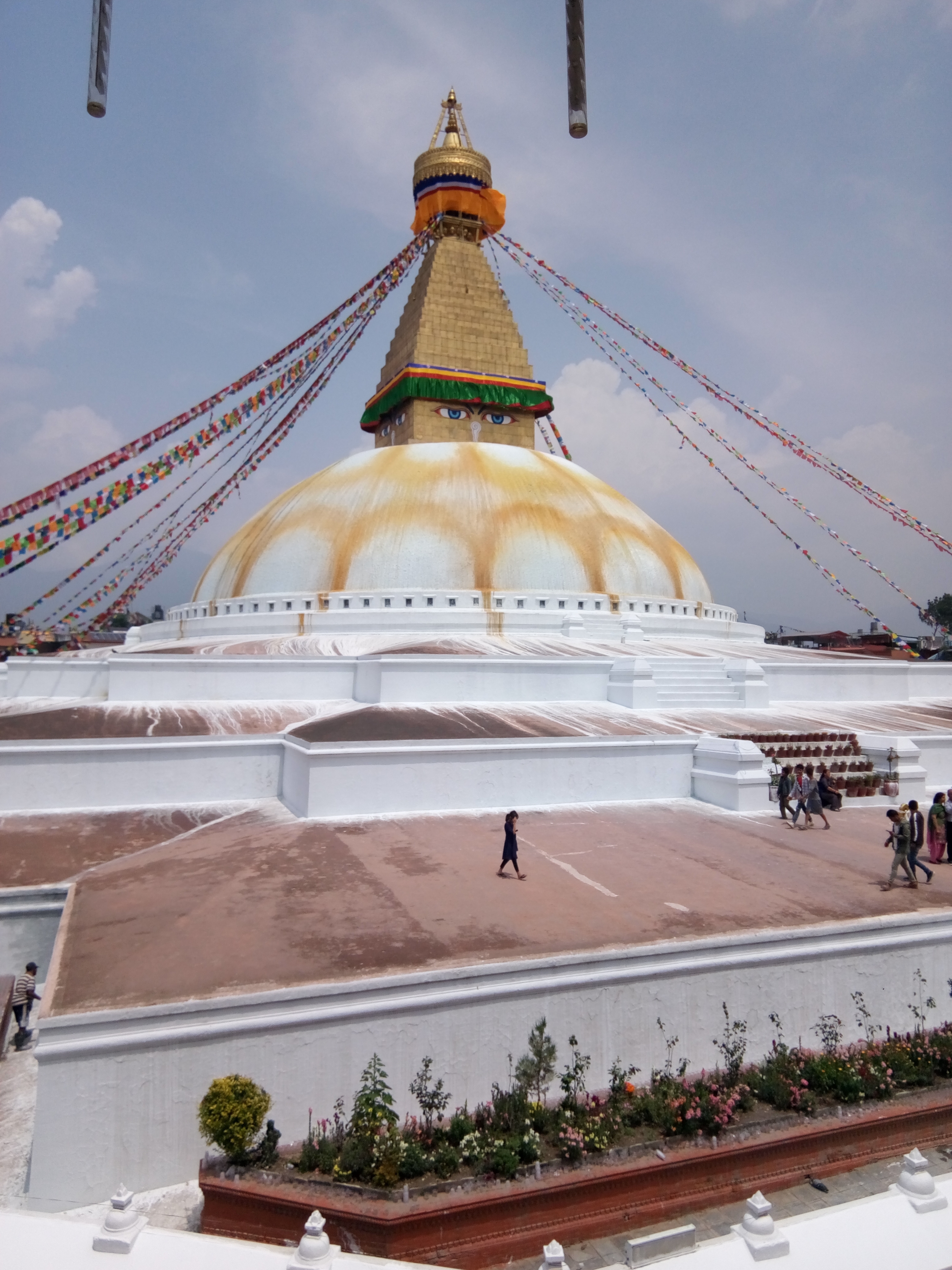 Large stupa with prayer flags and people walking around.