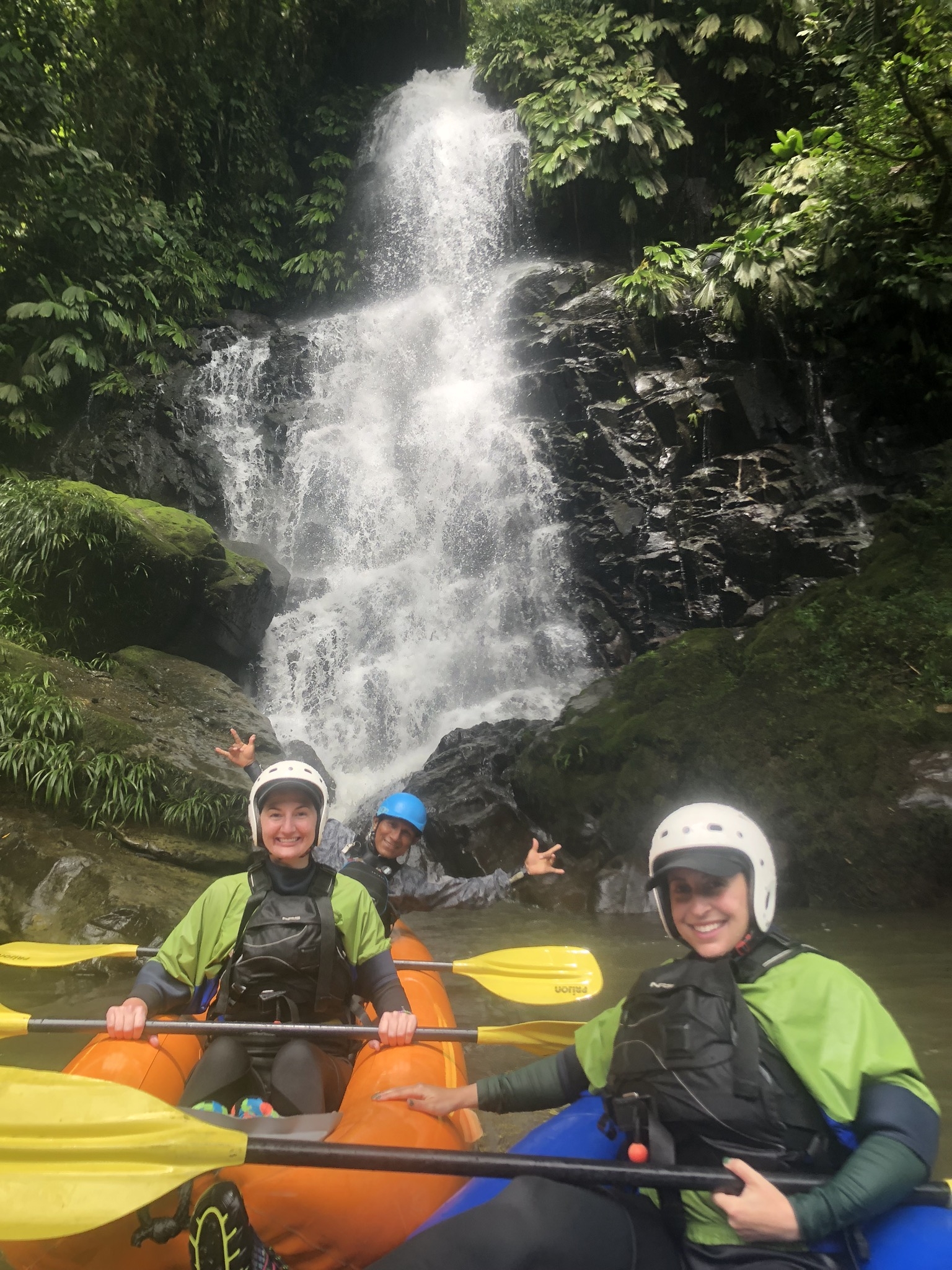 Group of people in front of a waterfall, wearing helmets.