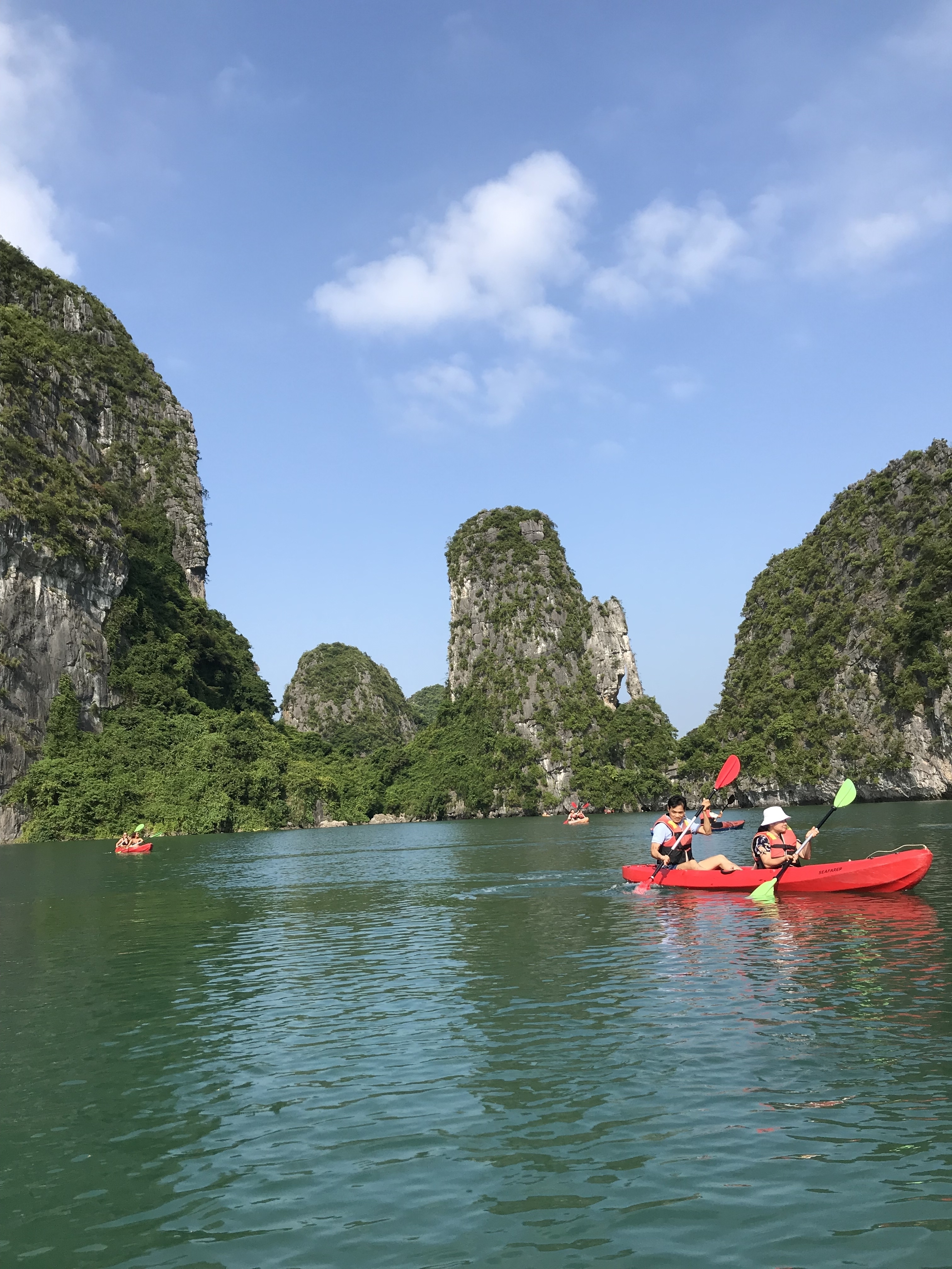 Kayakers paddling in a turquoise bay surrounded by limestone karsts.