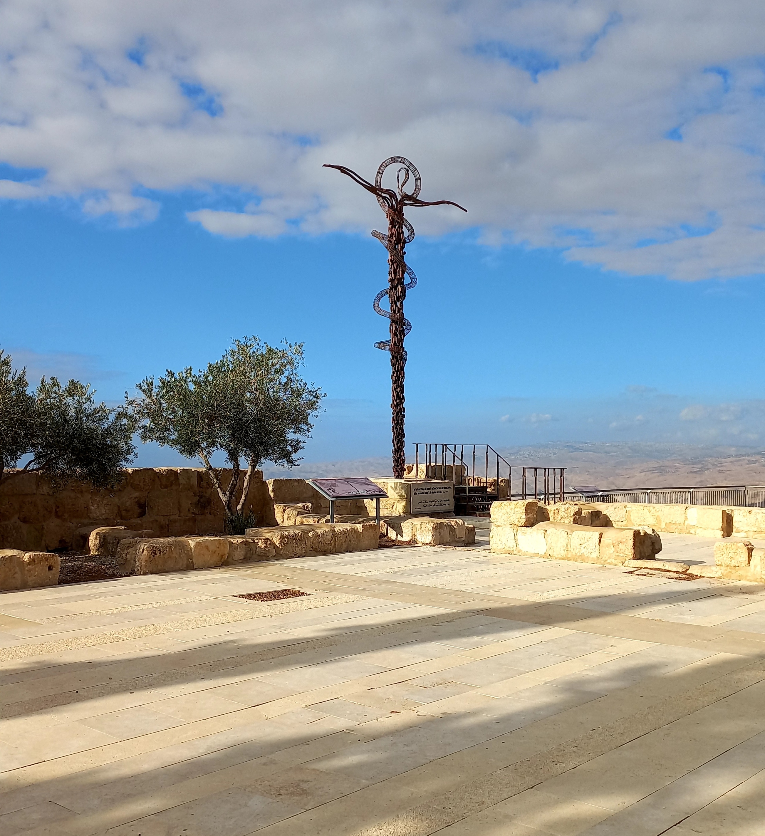Ancient structure with a serpent sculpture and trees in an open area under a blue sky.